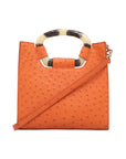 Front of a tangerine ostrich textured handbag with a strap on a white background