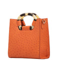 Side of a tangerine ostrich textured handbag on a white background