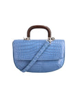 Front of a blue crocodile handbag with a strap and wooden handle on a white background