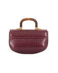 Back of a maroon crocodile handbag with a wooden handle on a white background