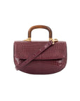 Front of a maroon crocodile handbag with a wooden handle on a white background