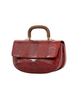 Side of a red textured handbag with gold accents and a wooden handle on a white background