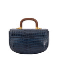 Back of a navy crocodile handbag with a wooden handle on a white background
