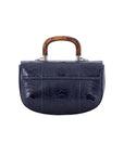 Back of a navy ostrich leg handbag with a strap and a wooden handle on a white background