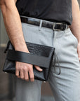 Person holding a black python clutch bag with textured pattern