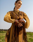 Woman in a brown outfit with a fringed brown suede bag standing in a field