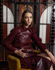 Woman in a burgundy leather outfit sitting on a yellow chair holding a burgundy crocodile leather handbag