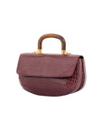 Side of a maroon crocodile handbag with a wooden handle on a white background