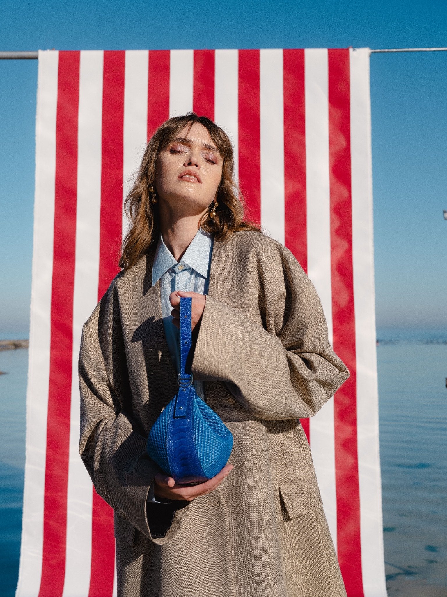 Women holding a woven blue handbag in front of a striped background