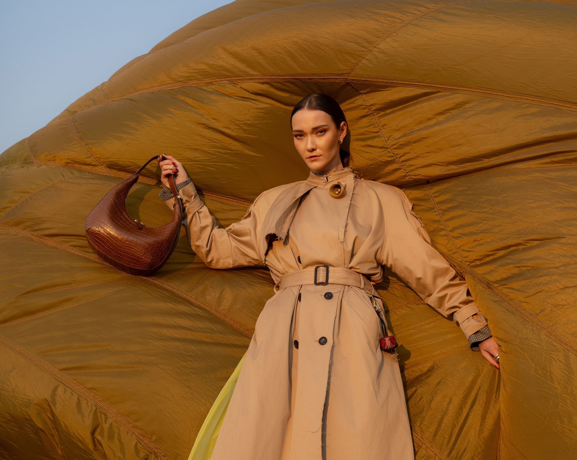 Woman in a beige trench coat holding a brown crocodile leather bag 