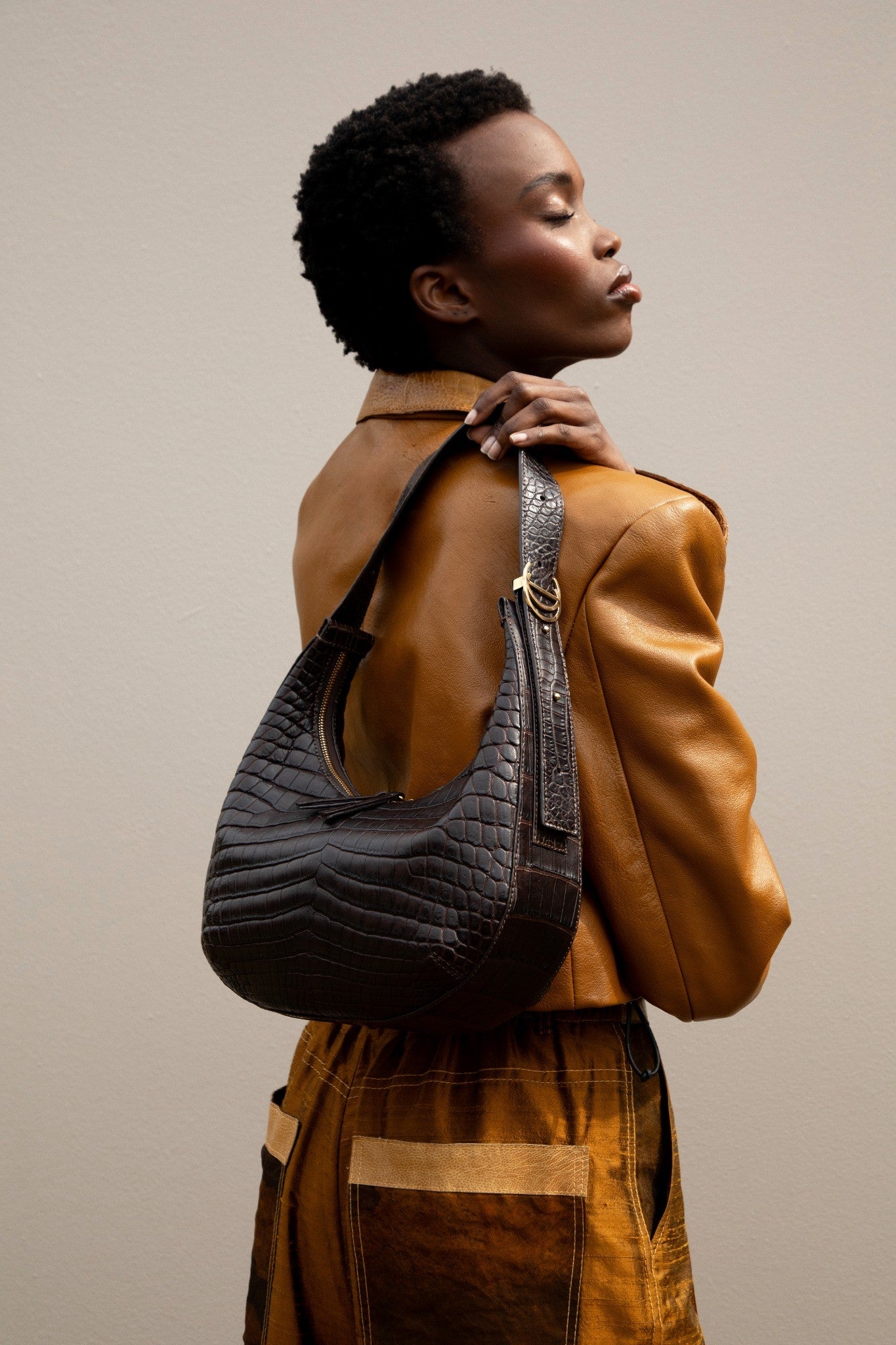 Woman wearing a brown crocodile handbag on a beige background