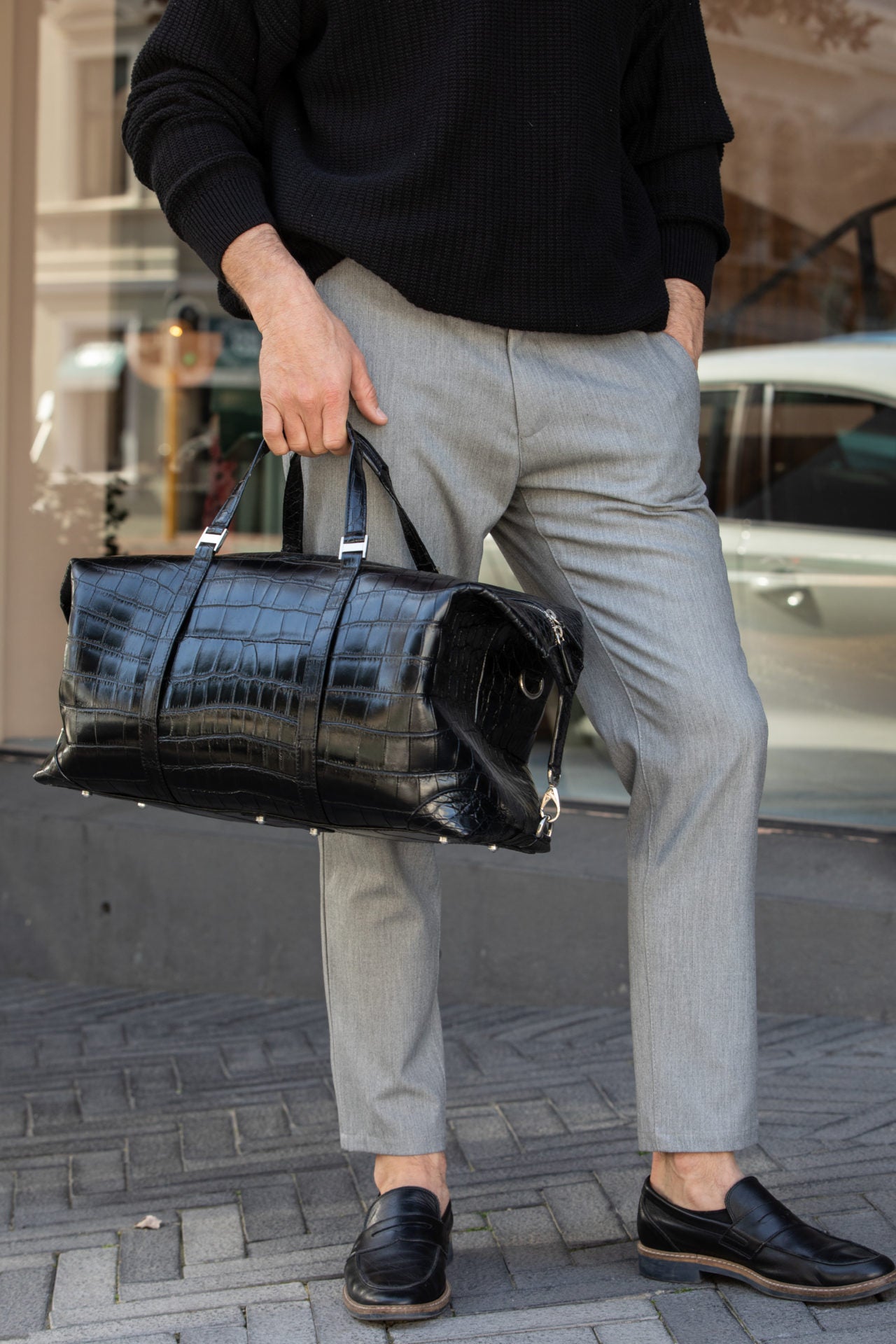 Person holding a black crocodile leather bag on a city street