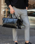 Person holding a black crocodile leather bag on a city street