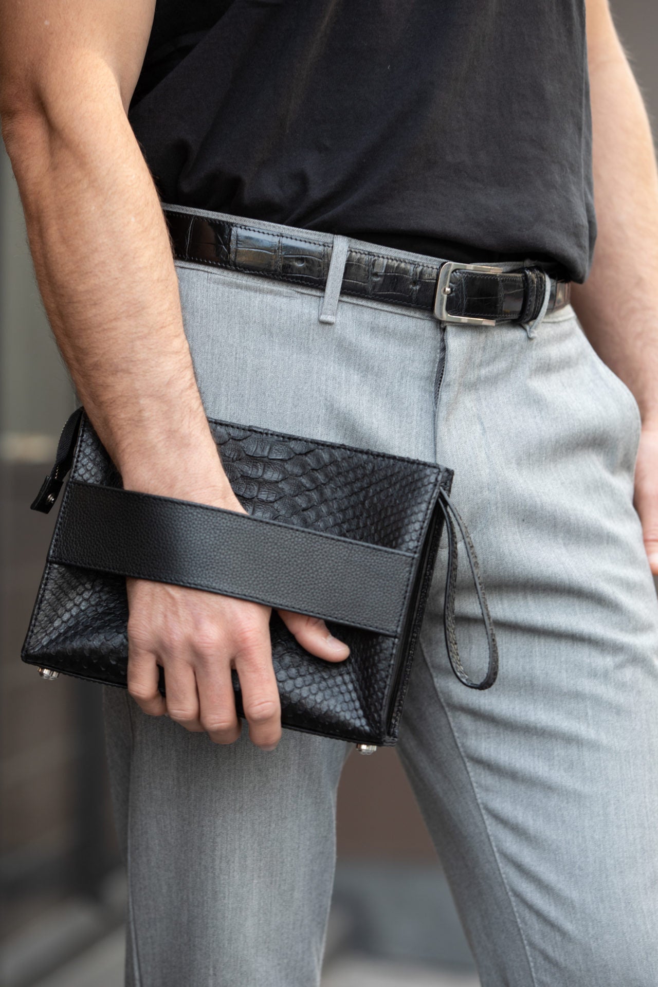 Person holding a black python clutch bag with textured pattern