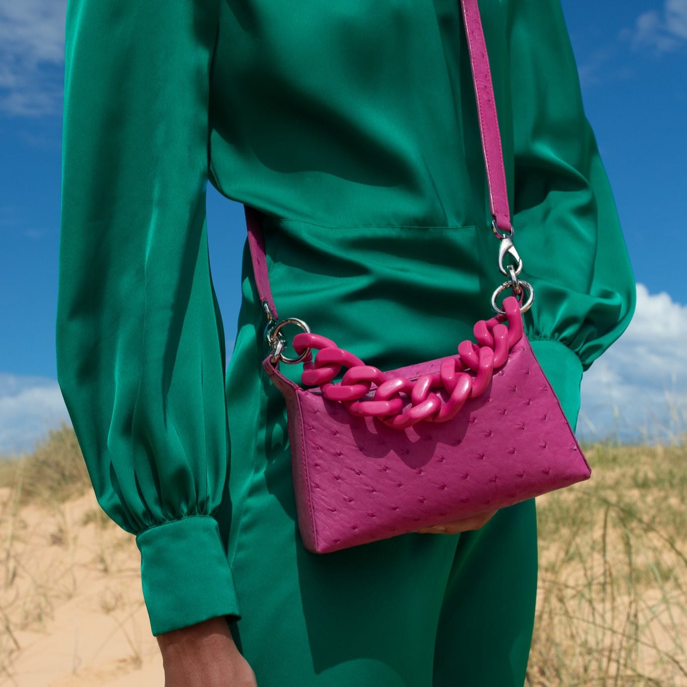 Person wearing a green outfit with a pink handbag against a blue sky.