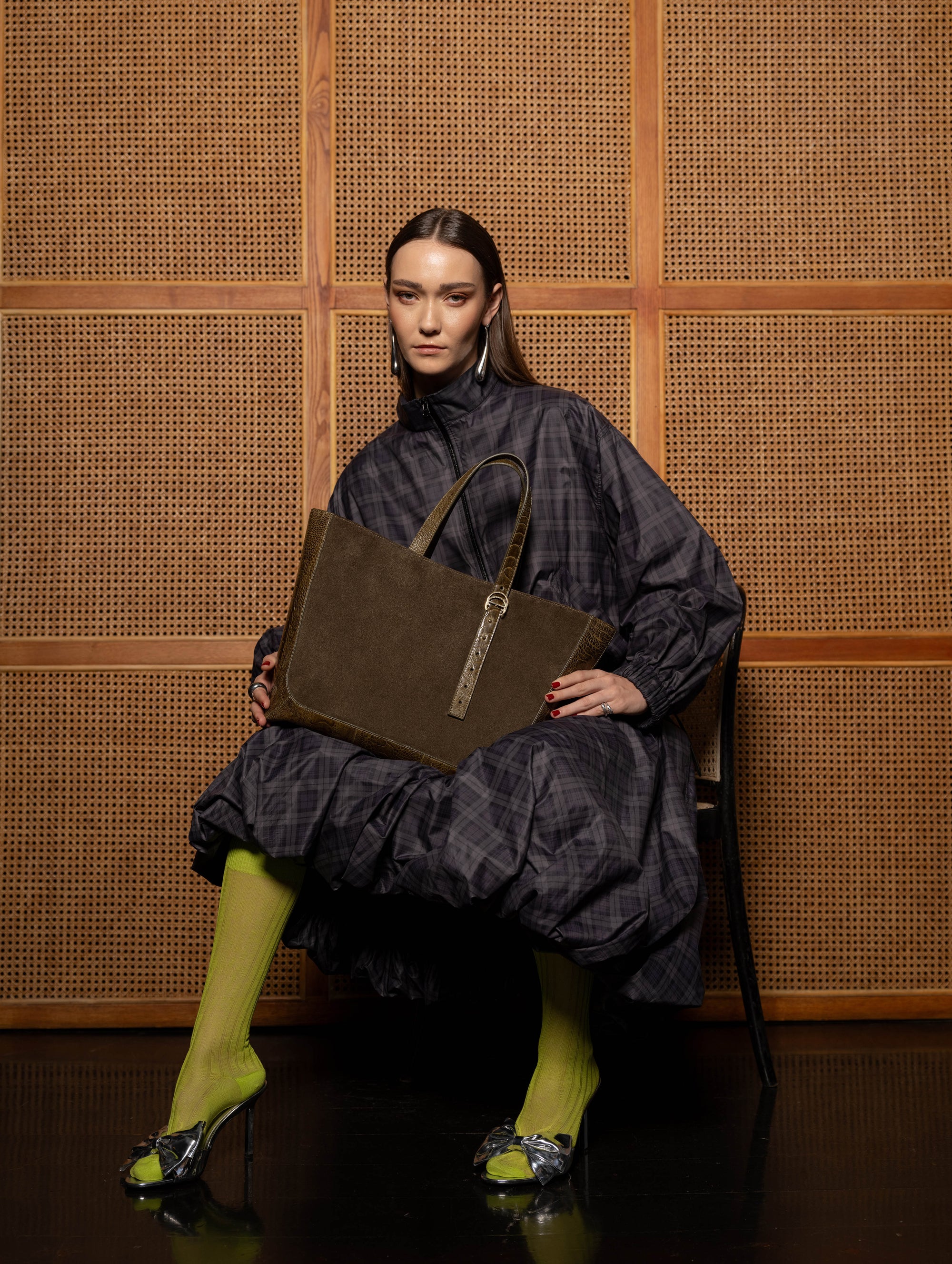 Woman holding a brown semi suede handbag against a woven wall
