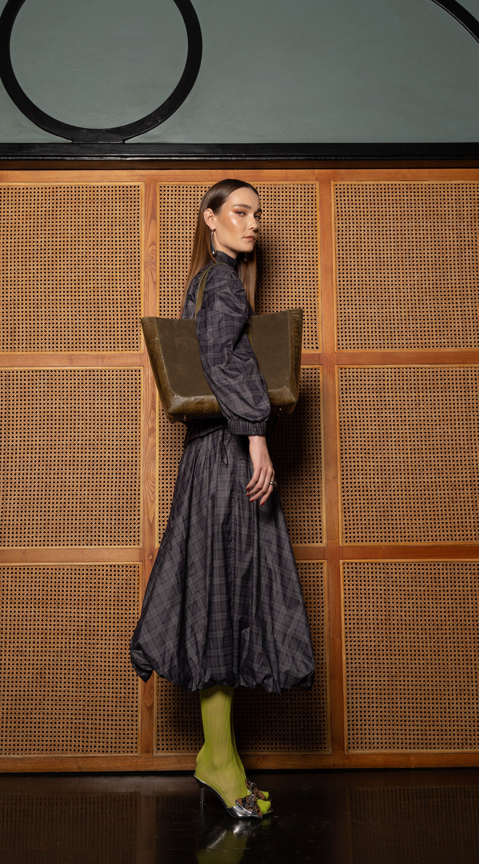 Woman in a dark dress standing holding a brown semi suede handbag