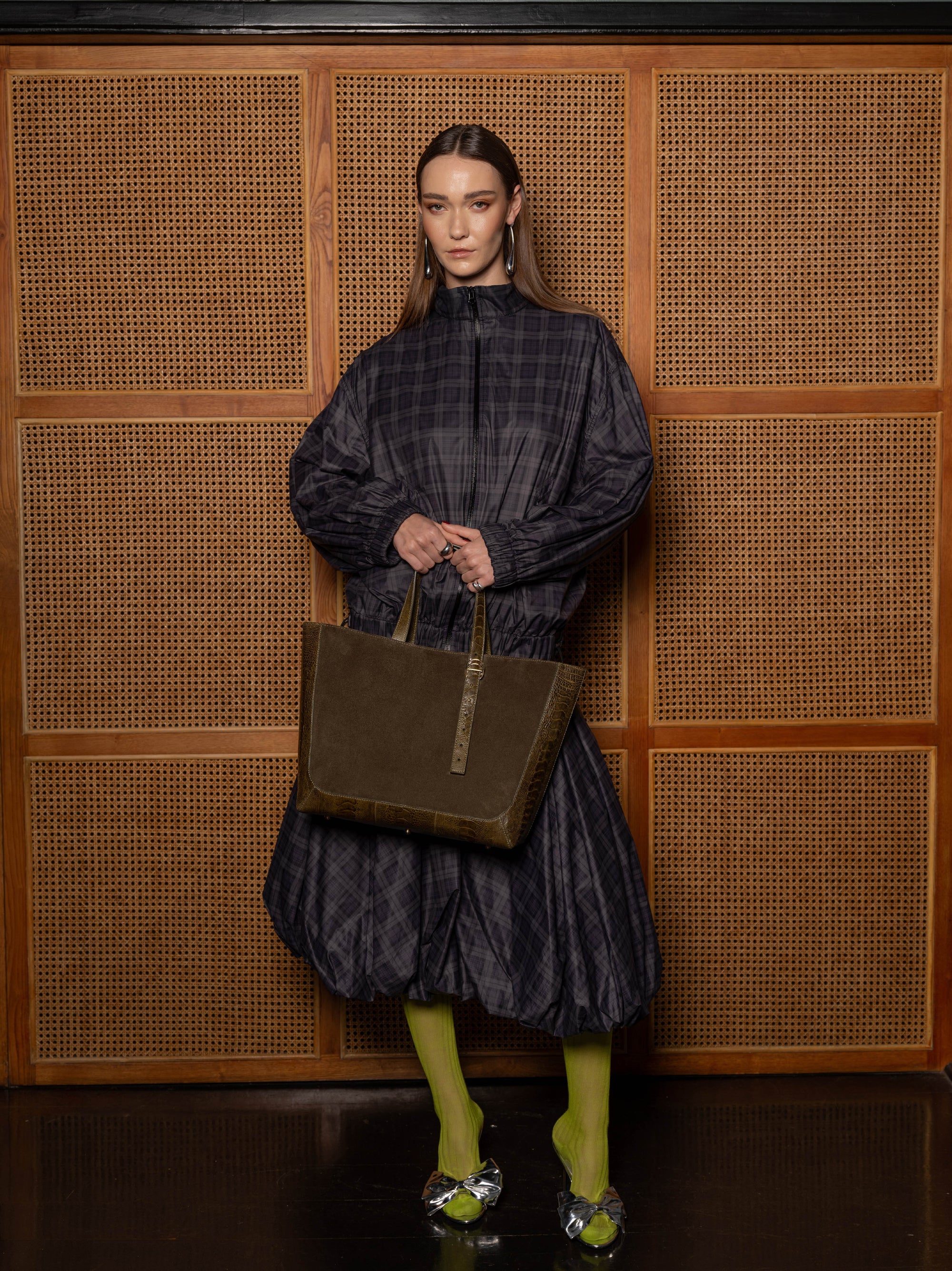 Person holding a brown suede tote bag against a textured wall.