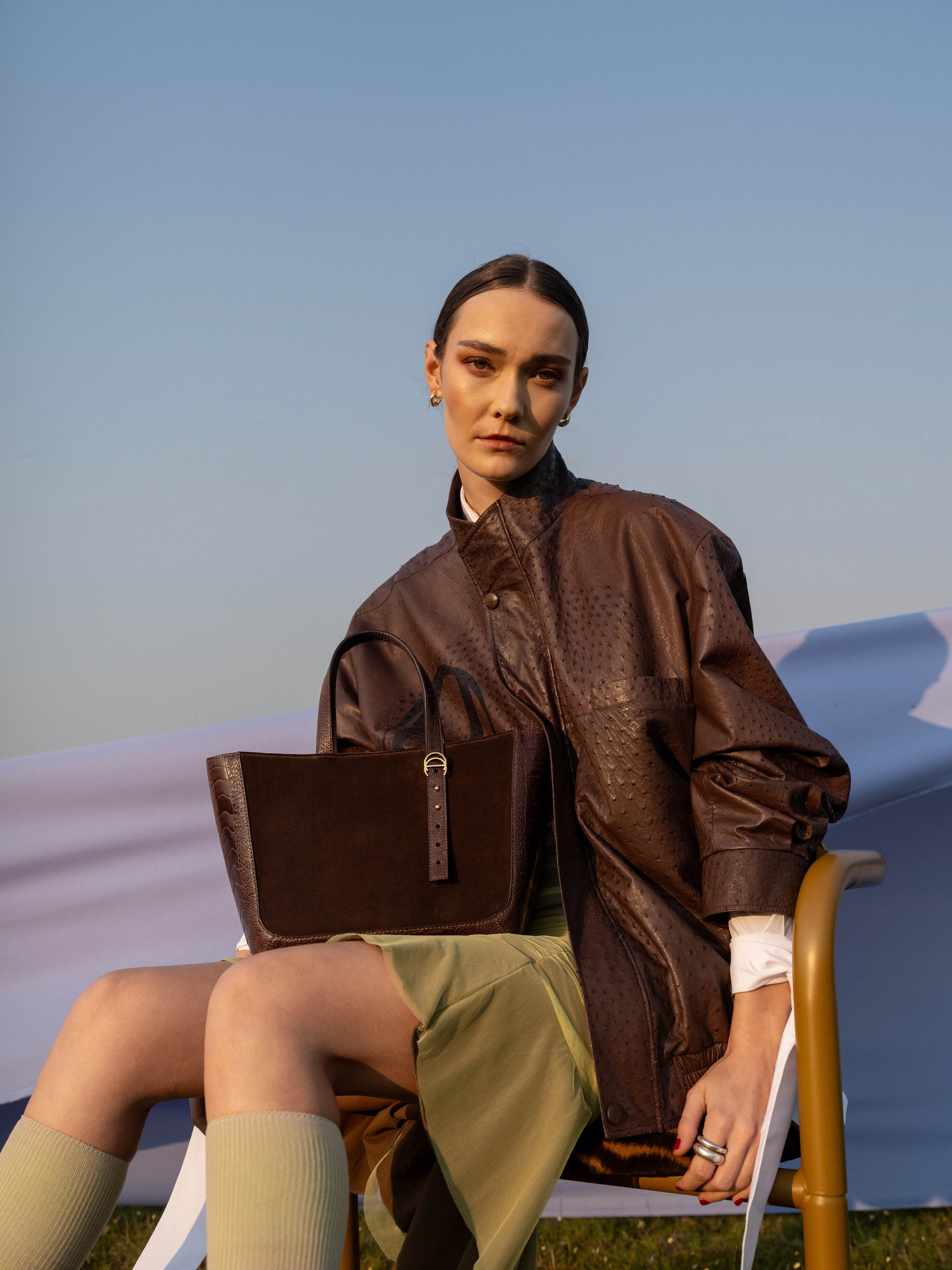 Woman sitting on a chair holding a brown semi suede handbag