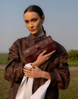 Woman holding a brown leather bag in an outdoor setting