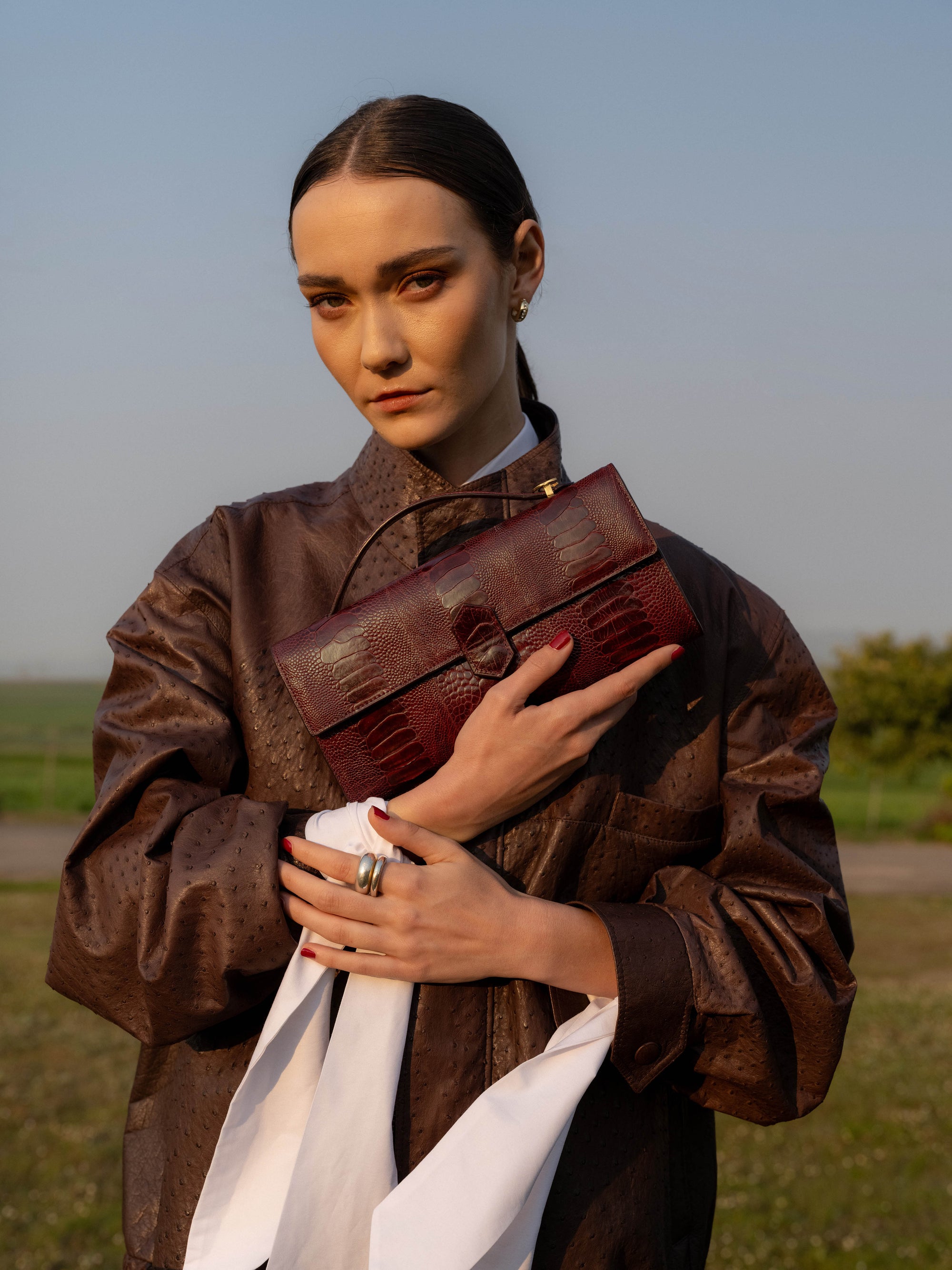Woman holding a brown leather bag in an outdoor setting