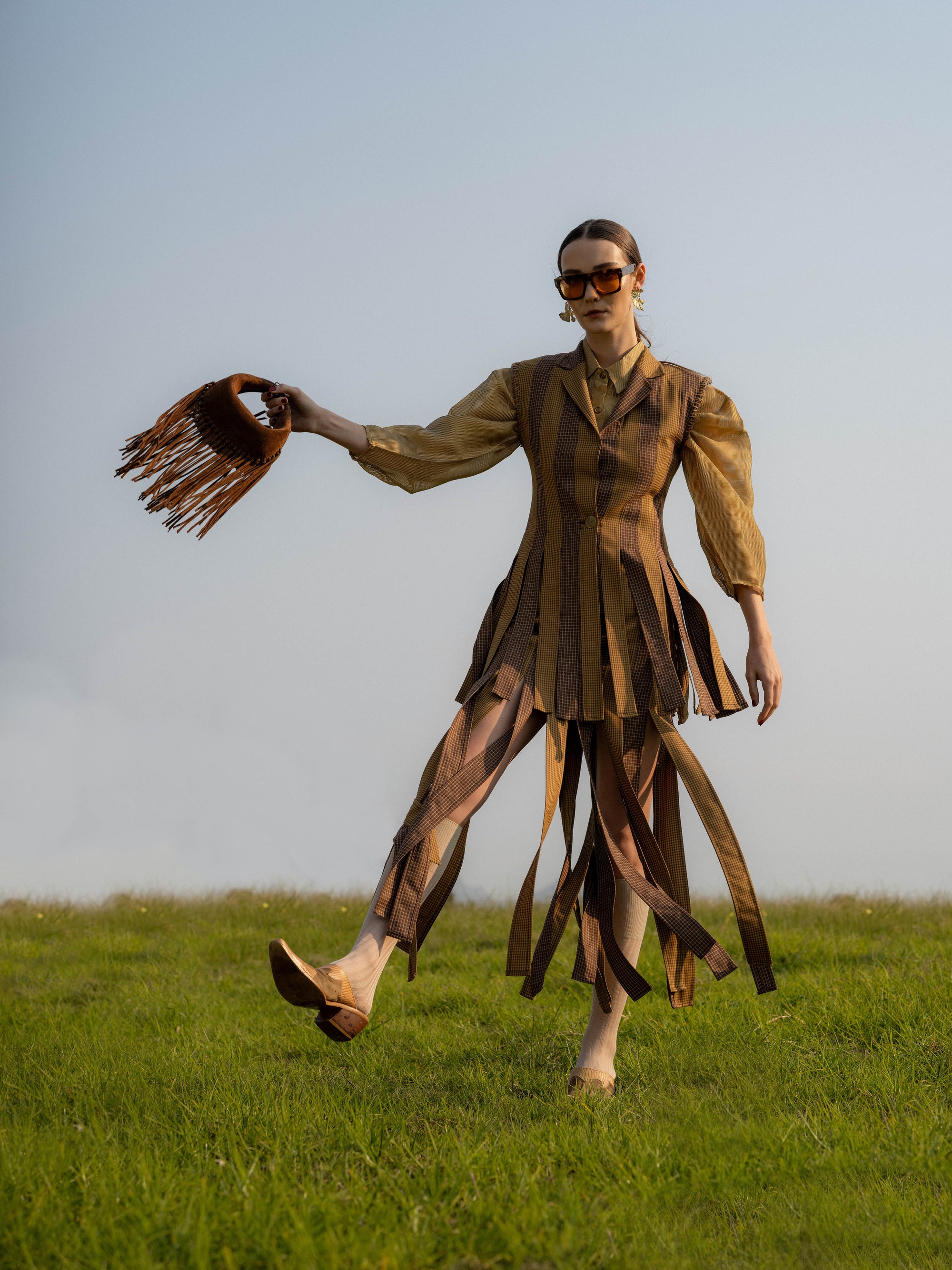 Woman in a brown outfit with a fringed brown suede bag standing in a field