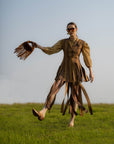 Woman in a brown outfit with a fringed brown suede bag standing in a field