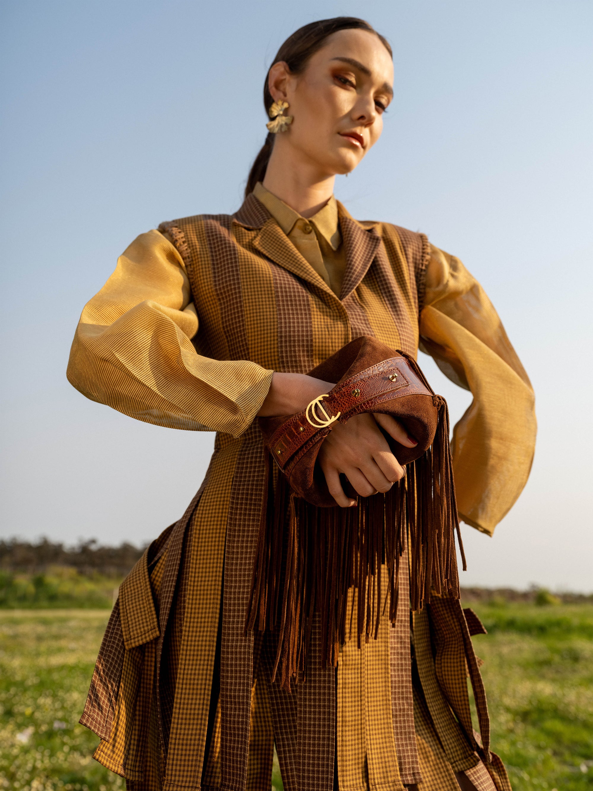 Woman in a brown outfit with a fringed brown suede bag standing in a field