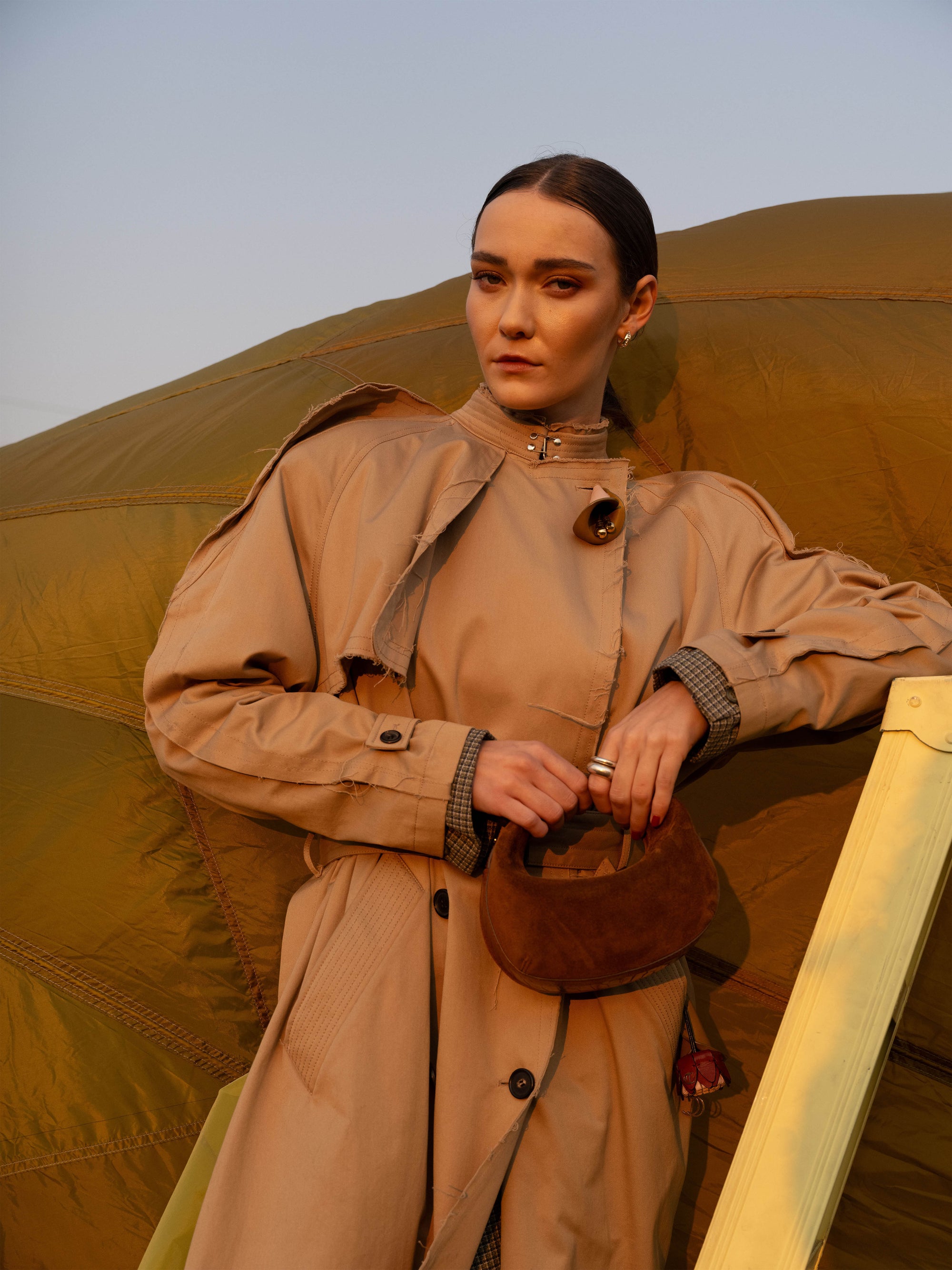 Person wearing a beige trench coat holding a brown suede handbag