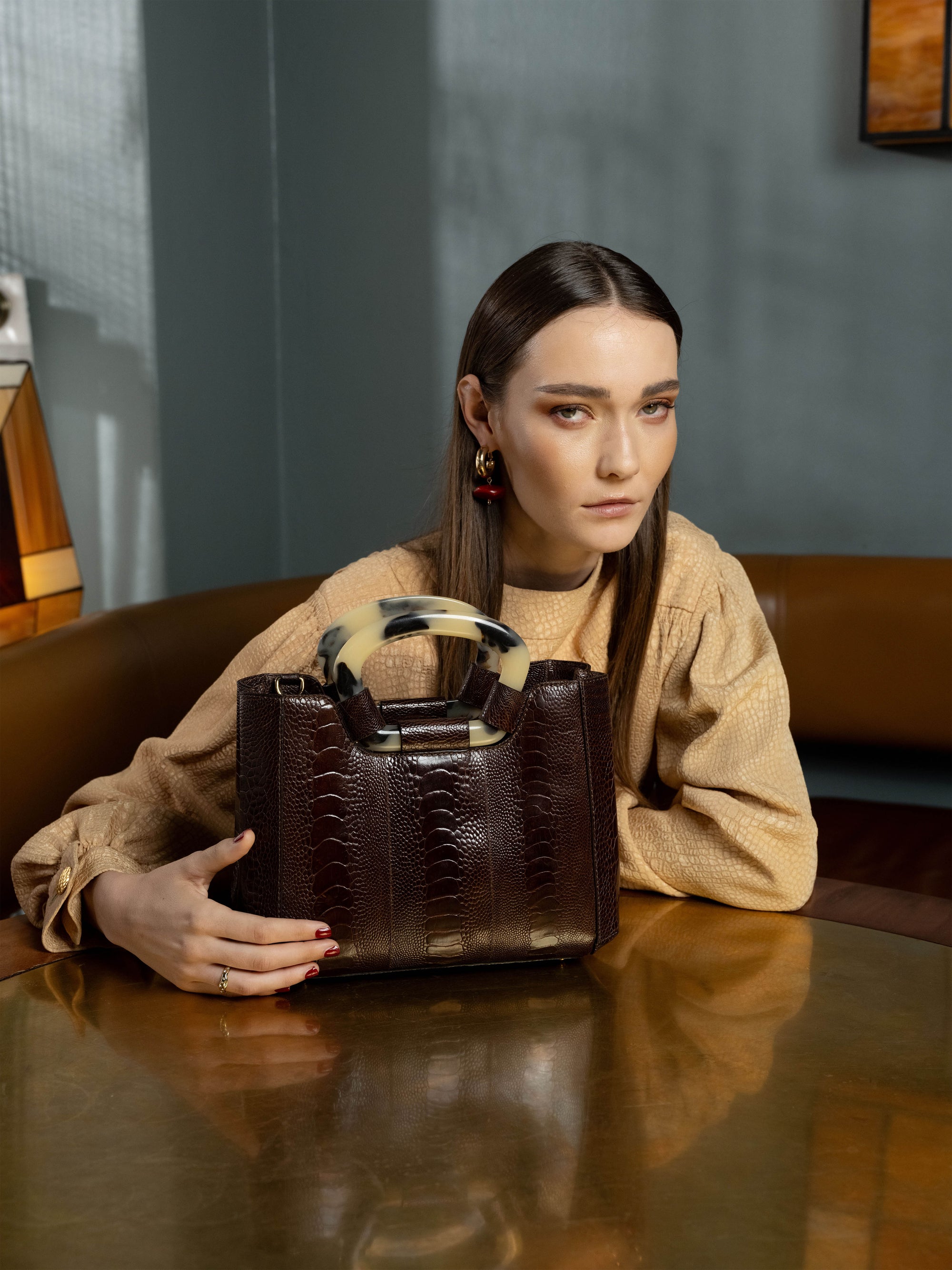 Woman holding a brown ostrich-leg textured handbag in an indoor setting