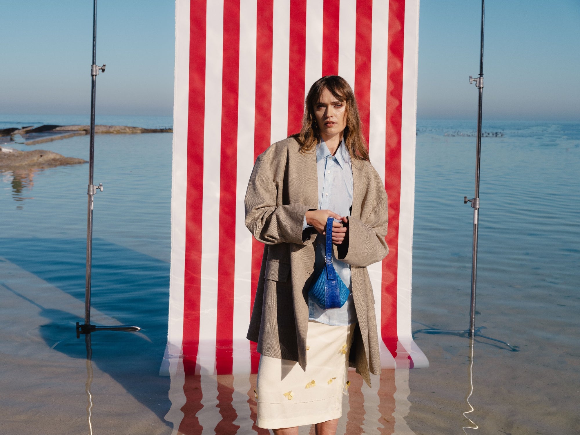 Woman holding a blue woven bag in front of a striped red background