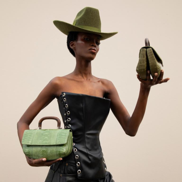 Model holding two green handbags against a neutral background