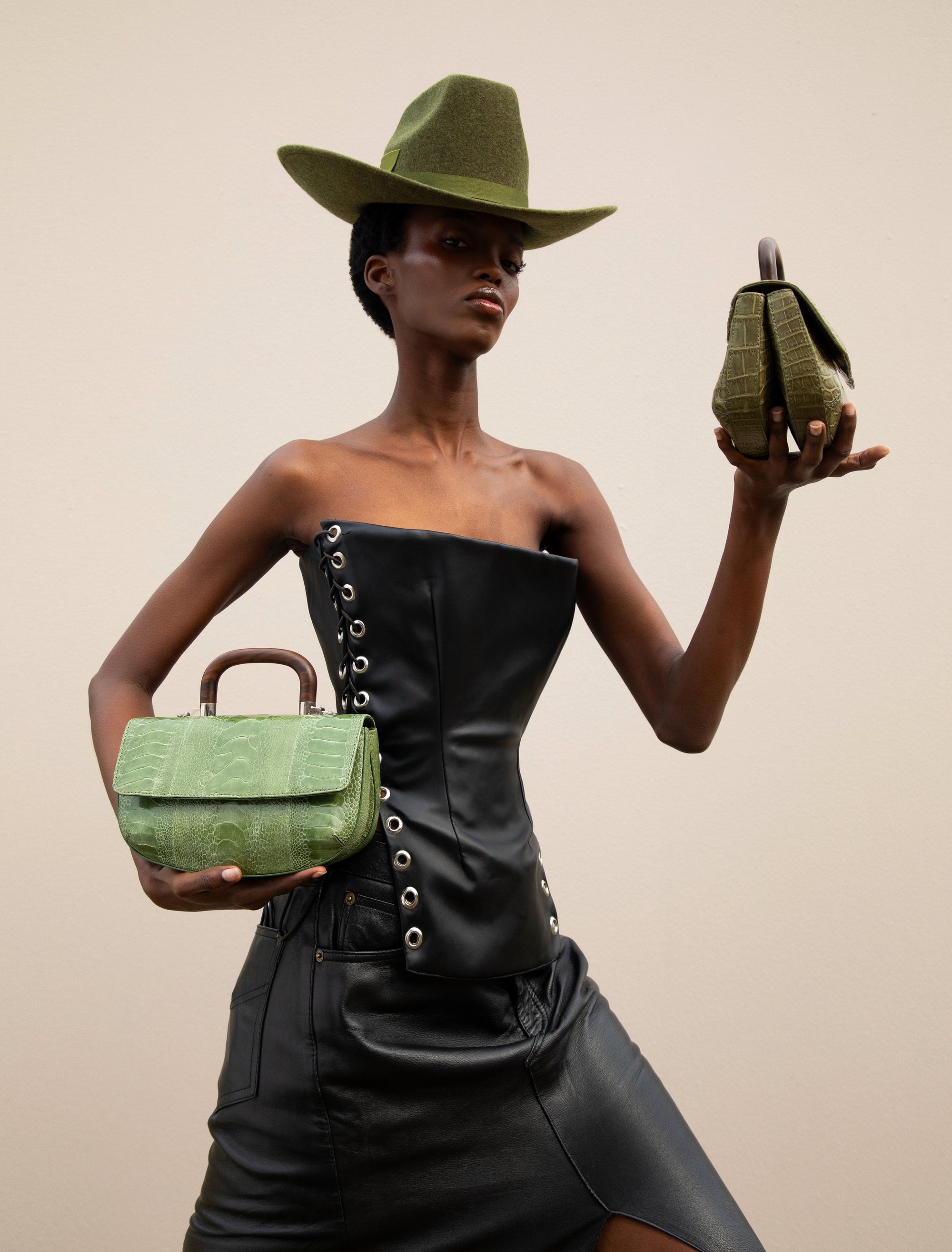 Woman holding a green handbag with a wooden handle in each hand against a neutral background