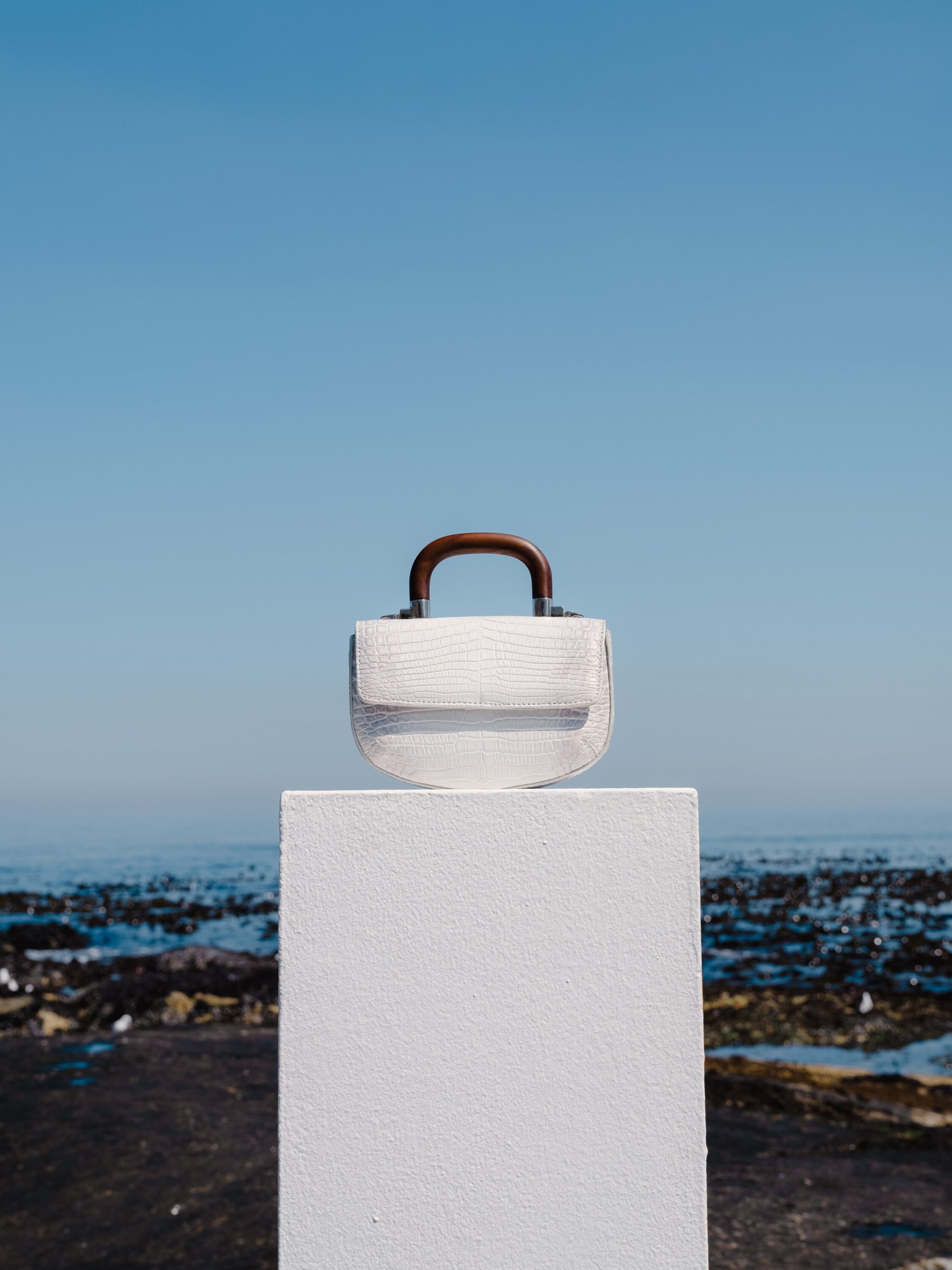 White handbag with wooden handle on a white pillar on ocean front