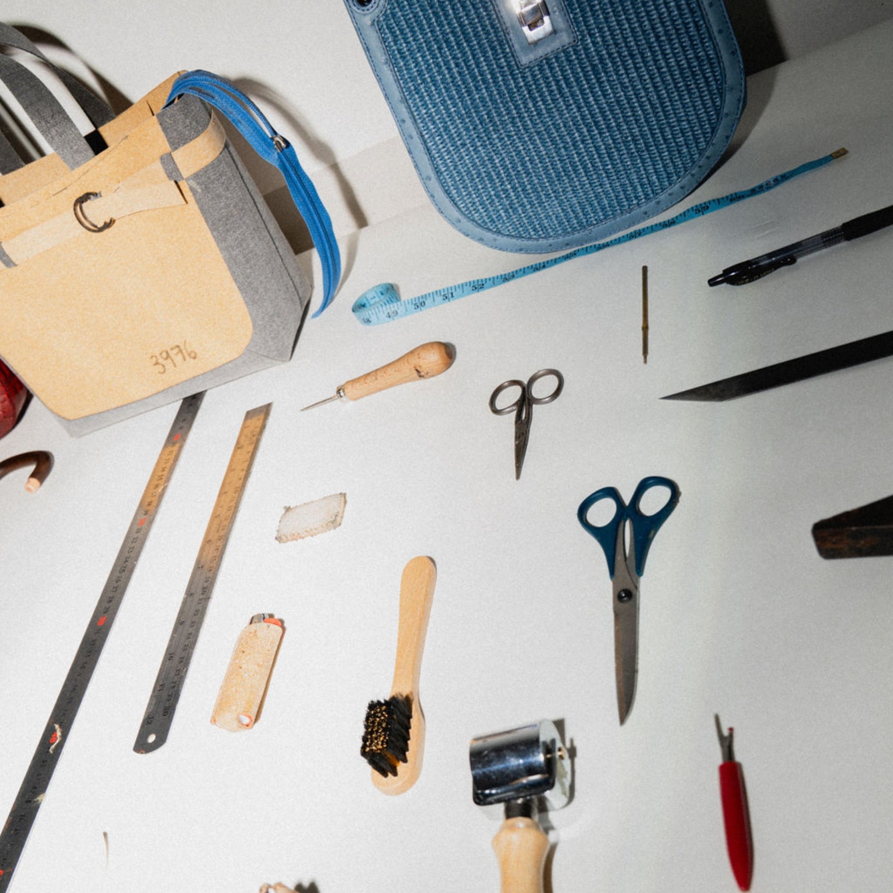 Assorted bag making tools including scissors, a ruler, brush and roller on a white surface.